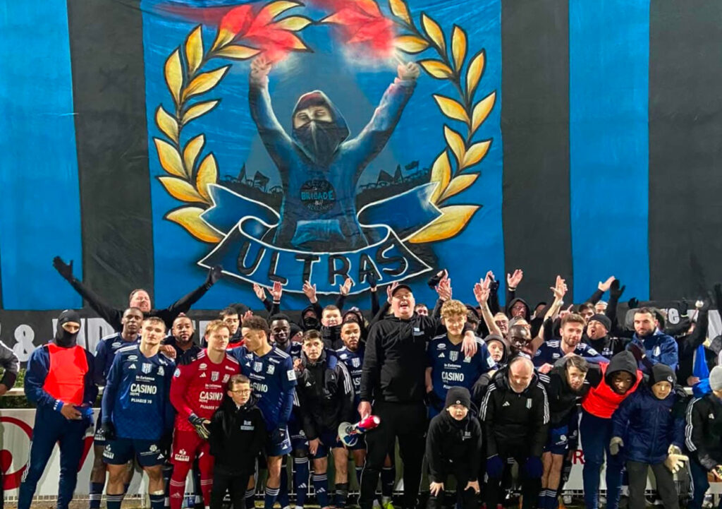 Les « Blue Herrings » posent avec les joueurs du FC Dieppe devant le premier tifo qu'ils ont confectionné dans leur (jeune) histoire.